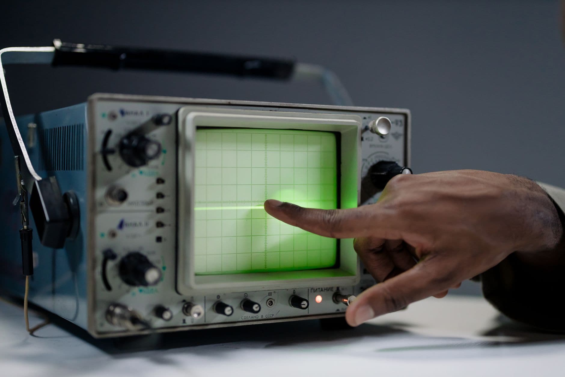 A hand pointing at the screen of a vintage oscilloscope.