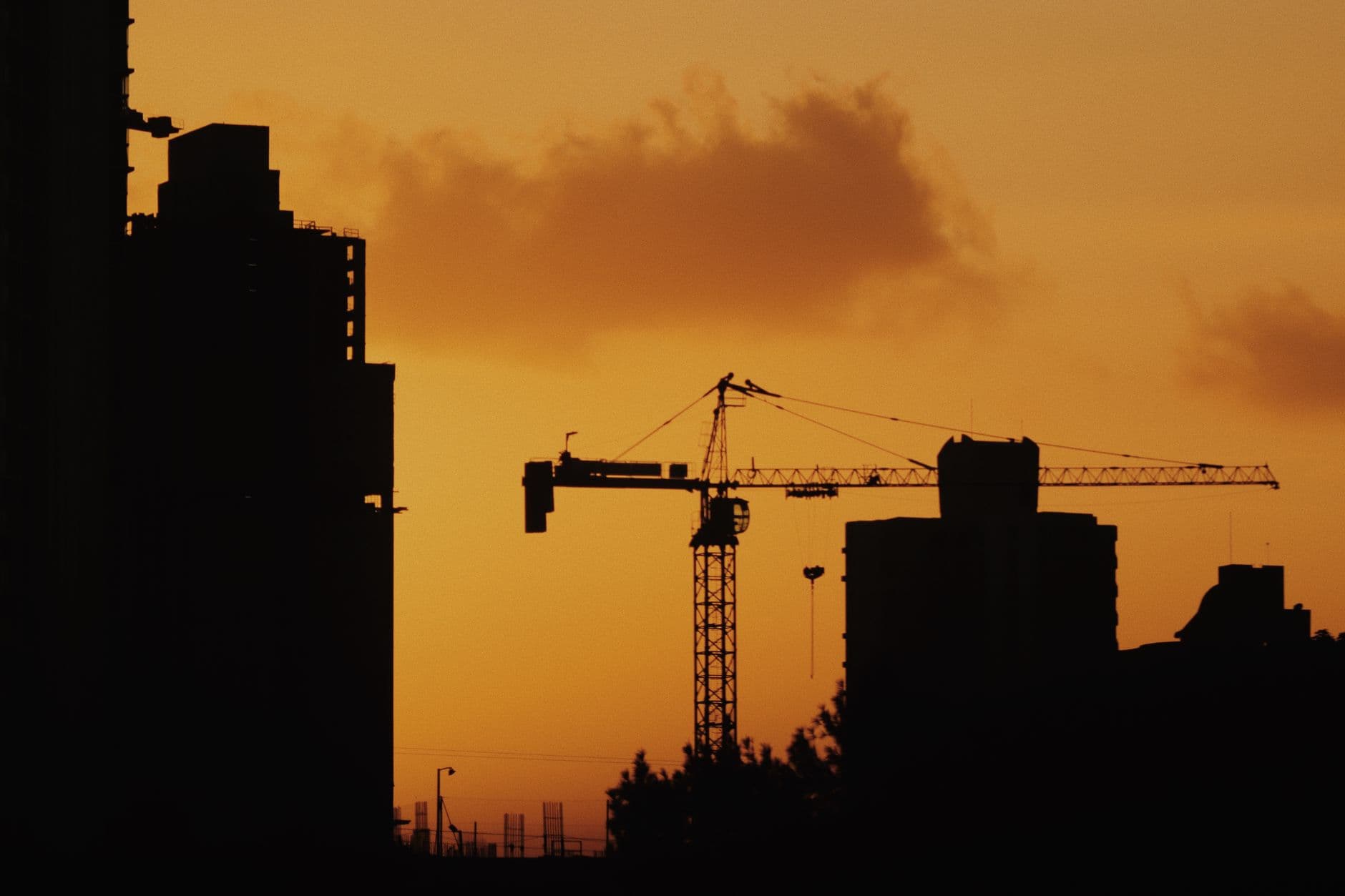 Silhouettes of cranes and buildings against a sunset sky.