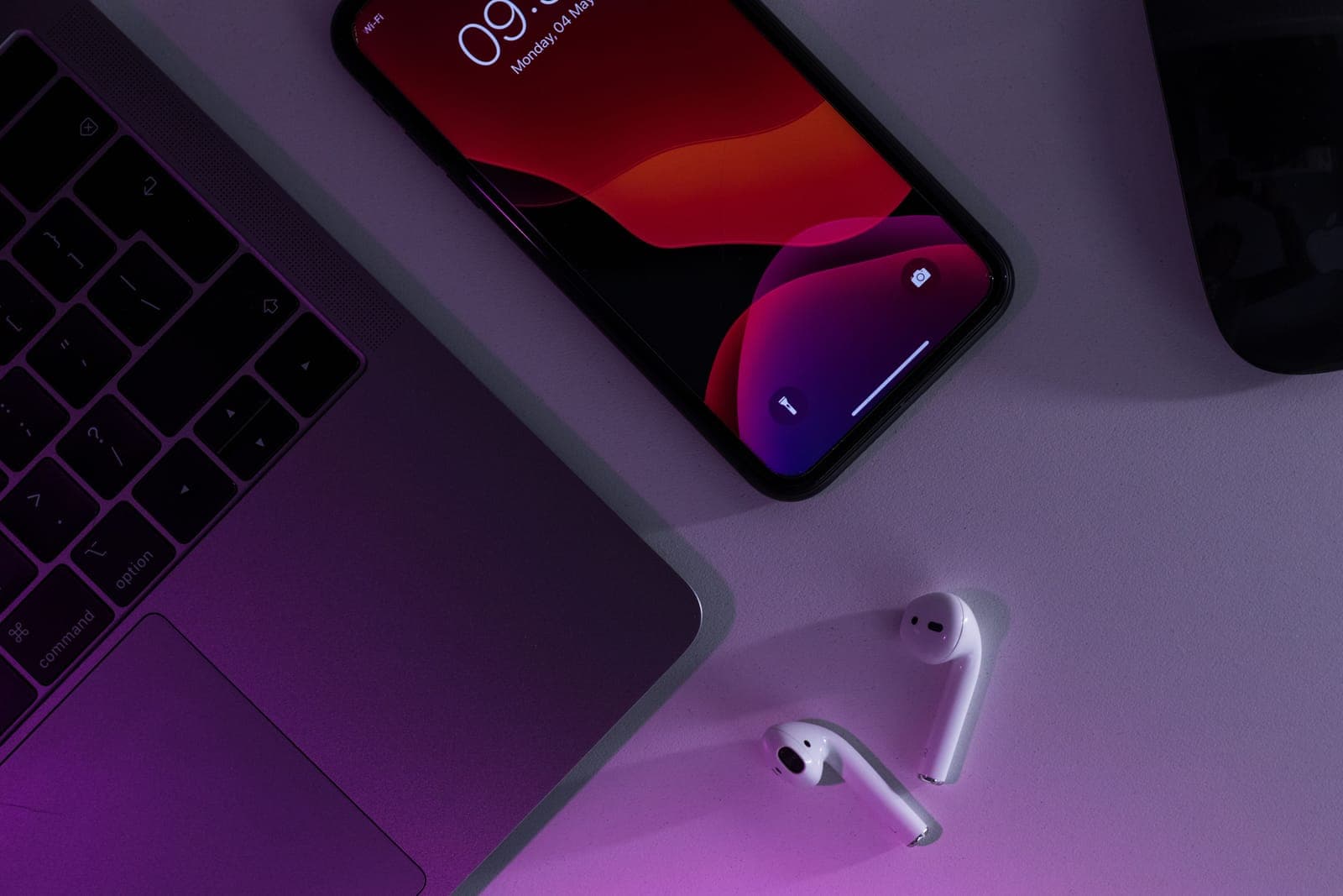 A laptop and phone on a desk in a dark room.