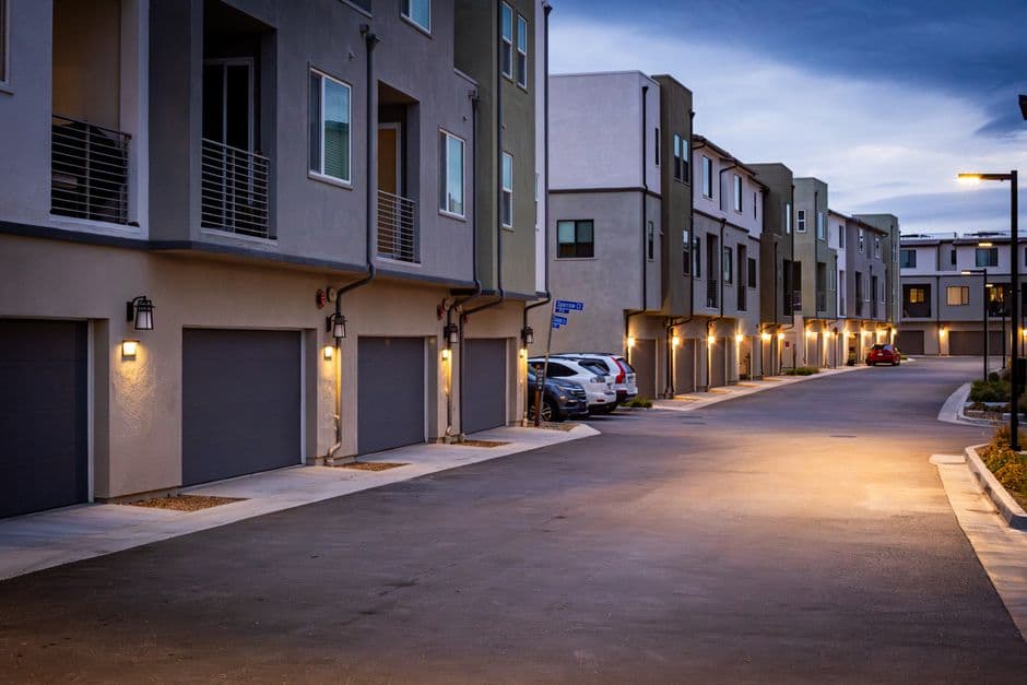 A suburban street with lit townhouses at dusk.