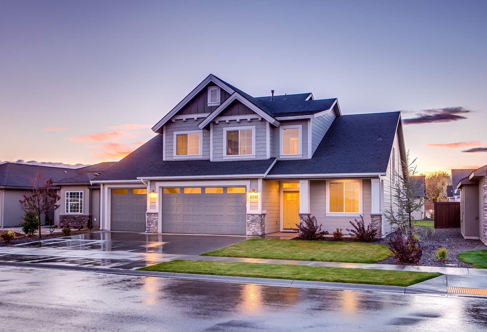 A large family house at dusk with its lights on.