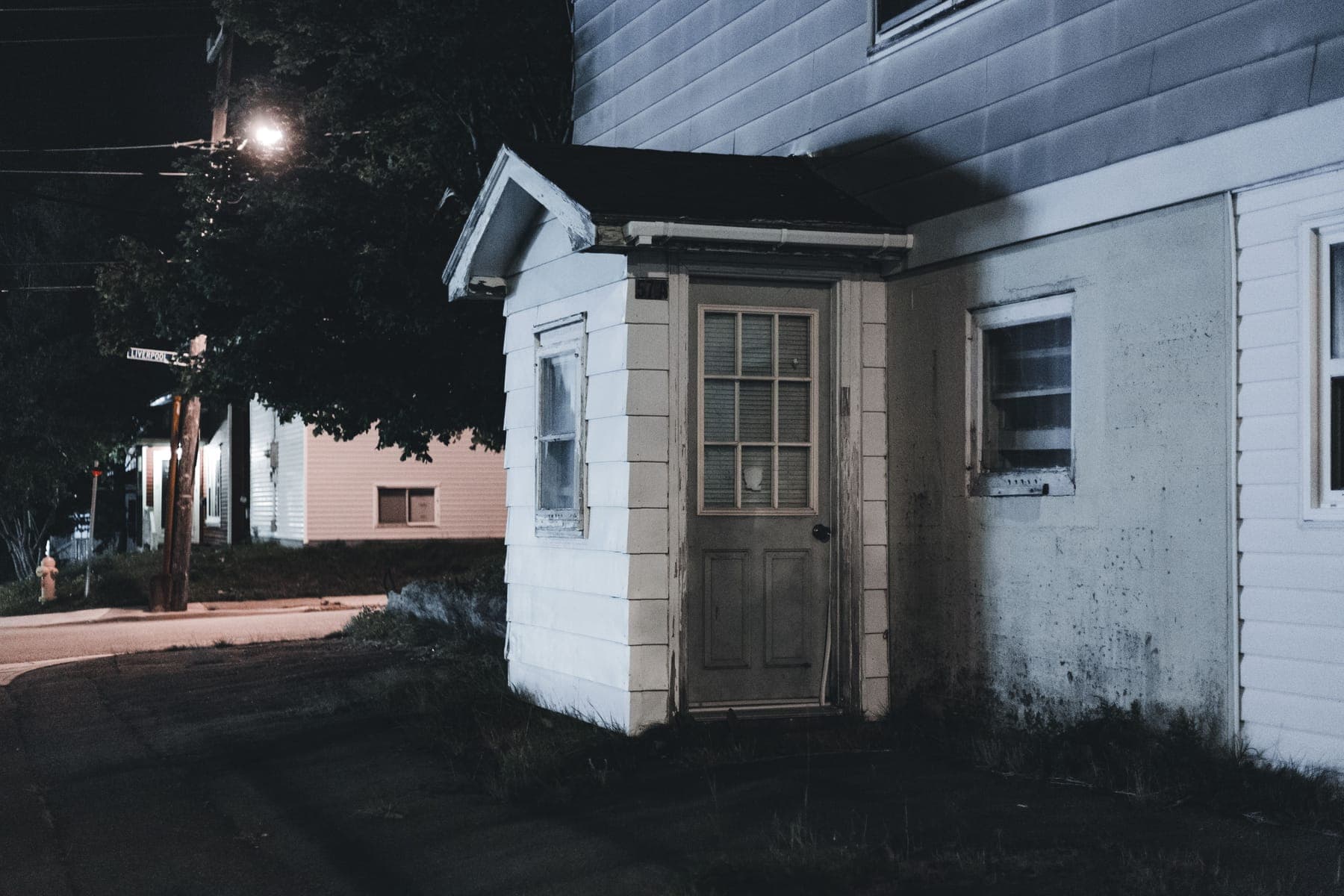 A dark suburban street at night with a single window lit in one house.