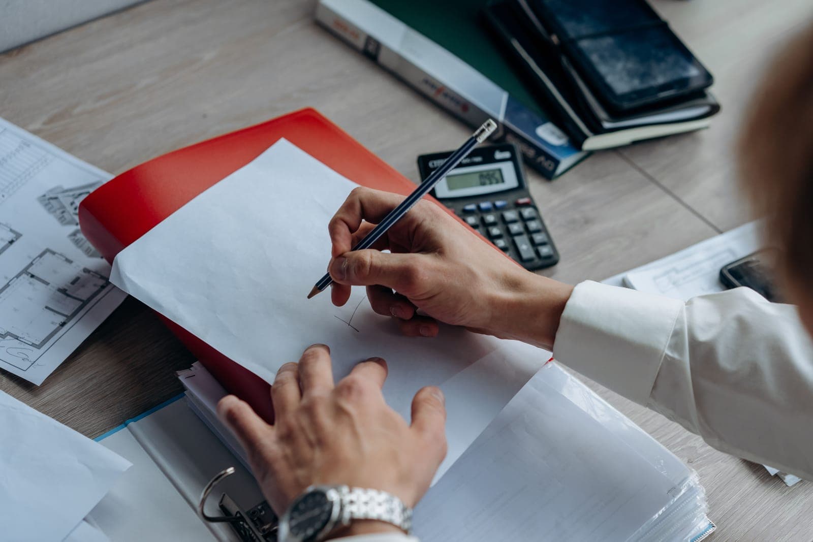 A notebook, calculator and wiring plan on a desk under a work lamp.